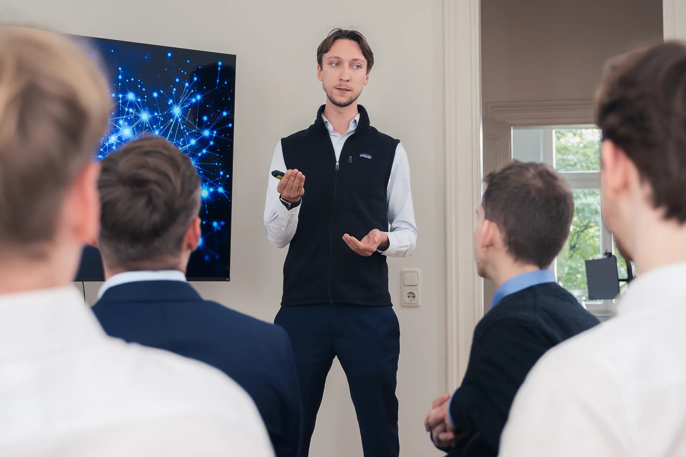 Ein BLAID-Seminar: ein Referent spricht zu einer sitzenden Gruppe, hinter ihm auf dem Bildschirm die Darstellung eines neuronalen Netzes.