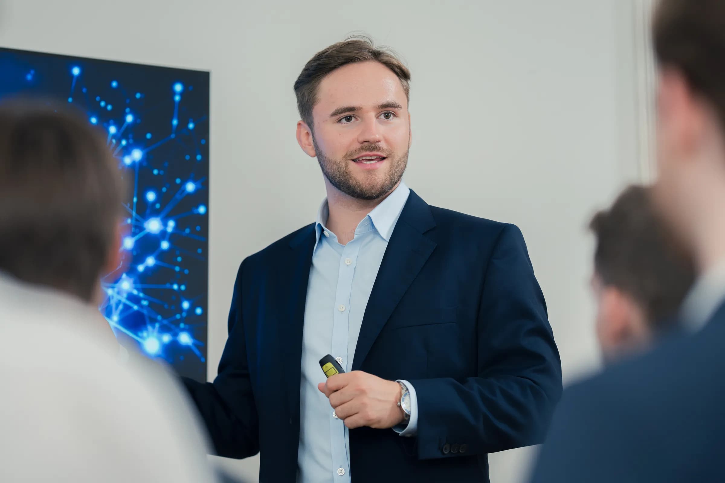 Ein BLAID-Strategieworkshop: ein Referent im Gespräch mit einer Gruppe, hinter ihm auf dem Bildschirm die Darstellung eines neuronalen Netzes.